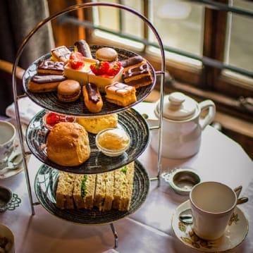 Image of an afternoon tea set with sandwiches, scones, patisserie and a cup of tea.